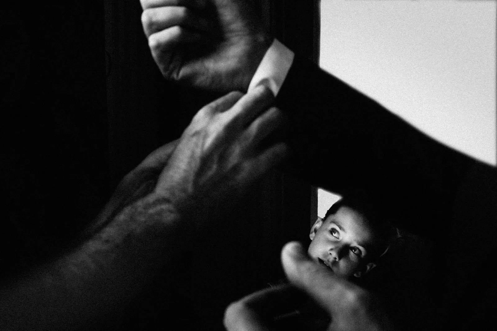 Hands straightening a tie while a child watches from below, in black and white