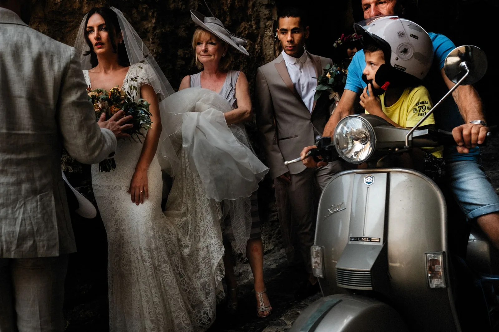 A bride, her family and a boy on a scooter crowded into a narrow stone alley
