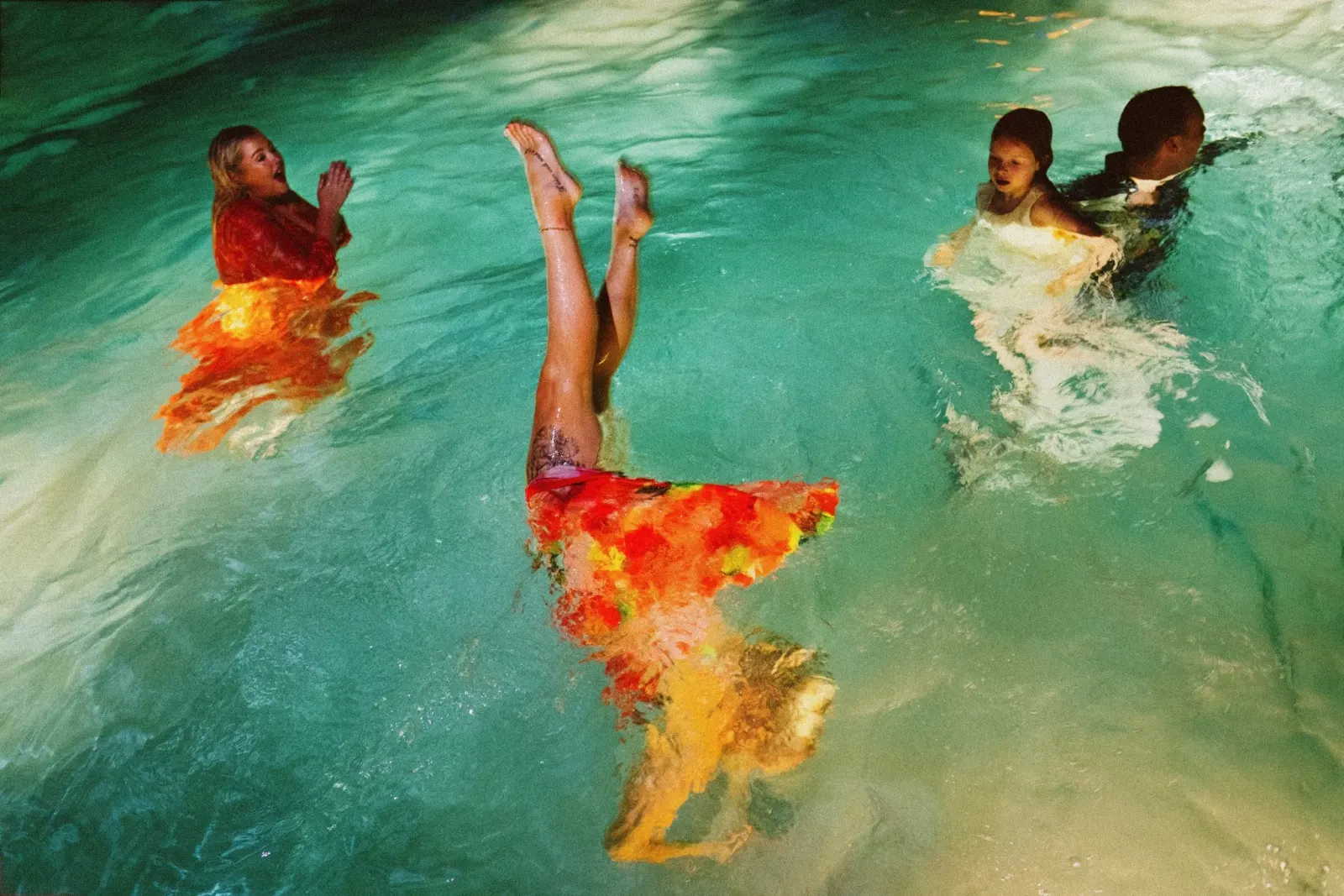 Guests swimming in a pool, a woman floating in an orange dress