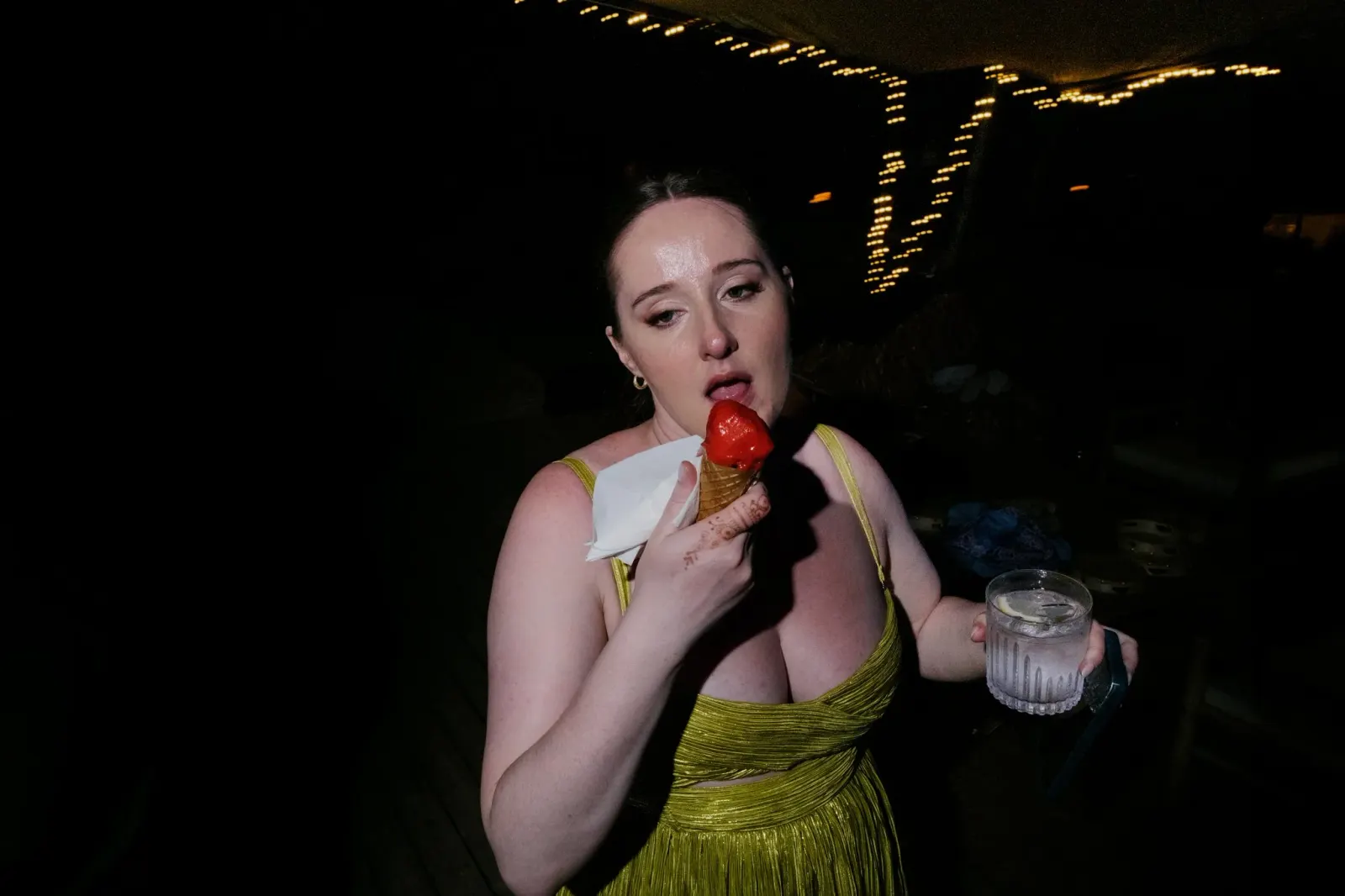 A guest in a green dress eating a strawberry ice lolly under string lights