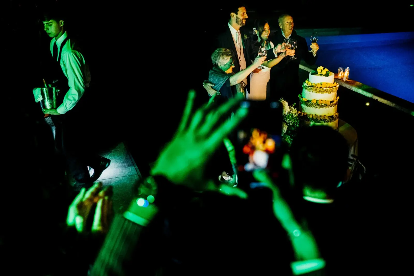 Hands raised in green laser light around the cake