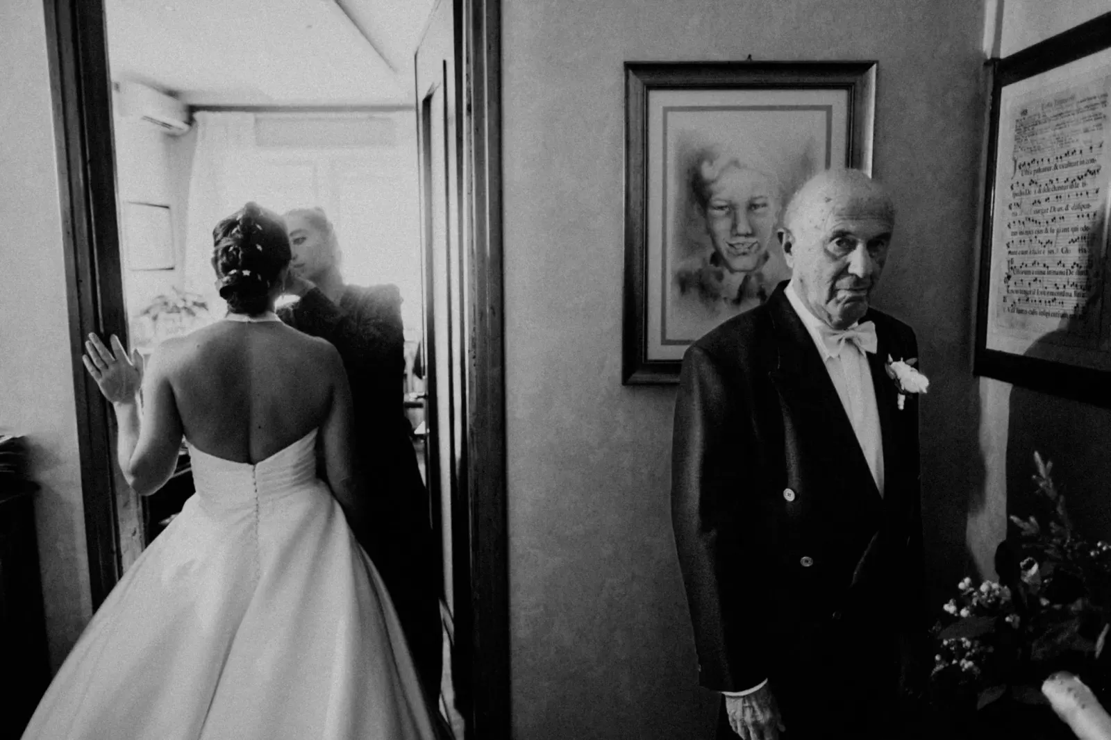 A bride turning towards an elderly man in tails in a narrow hallway
