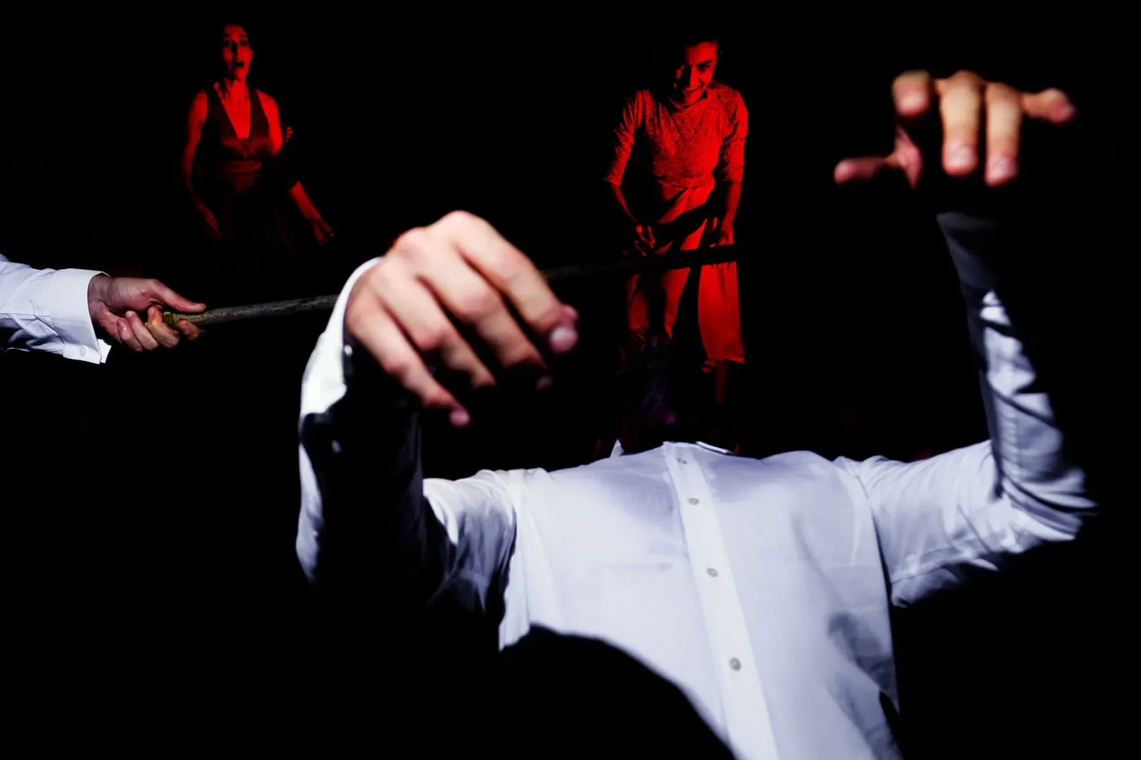 A man conducting with both hands raised, dancers in red behind him