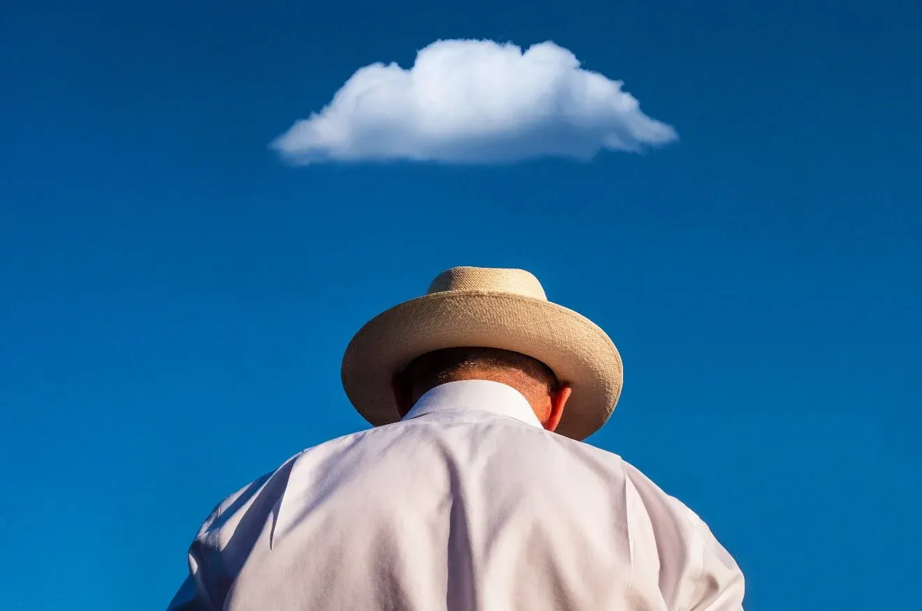 A man in a straw hat seen from below against a single cloud