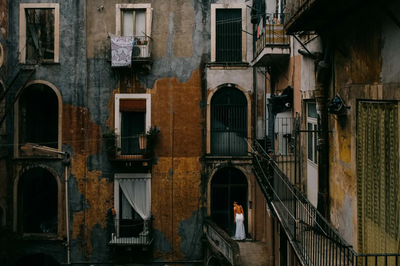 A woman at a window above a narrow street of peeling balconies