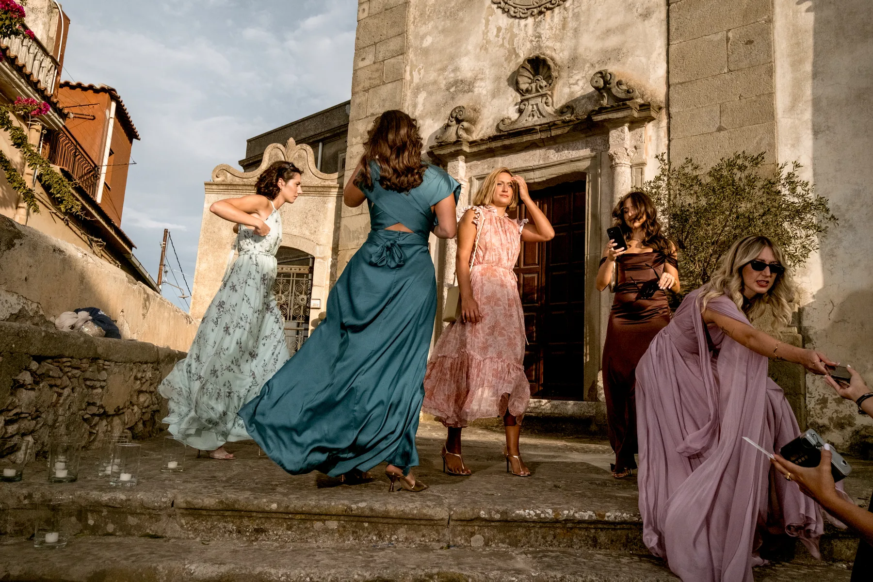 Bridesmaids in long dresses blown by the wind on the steps of a church