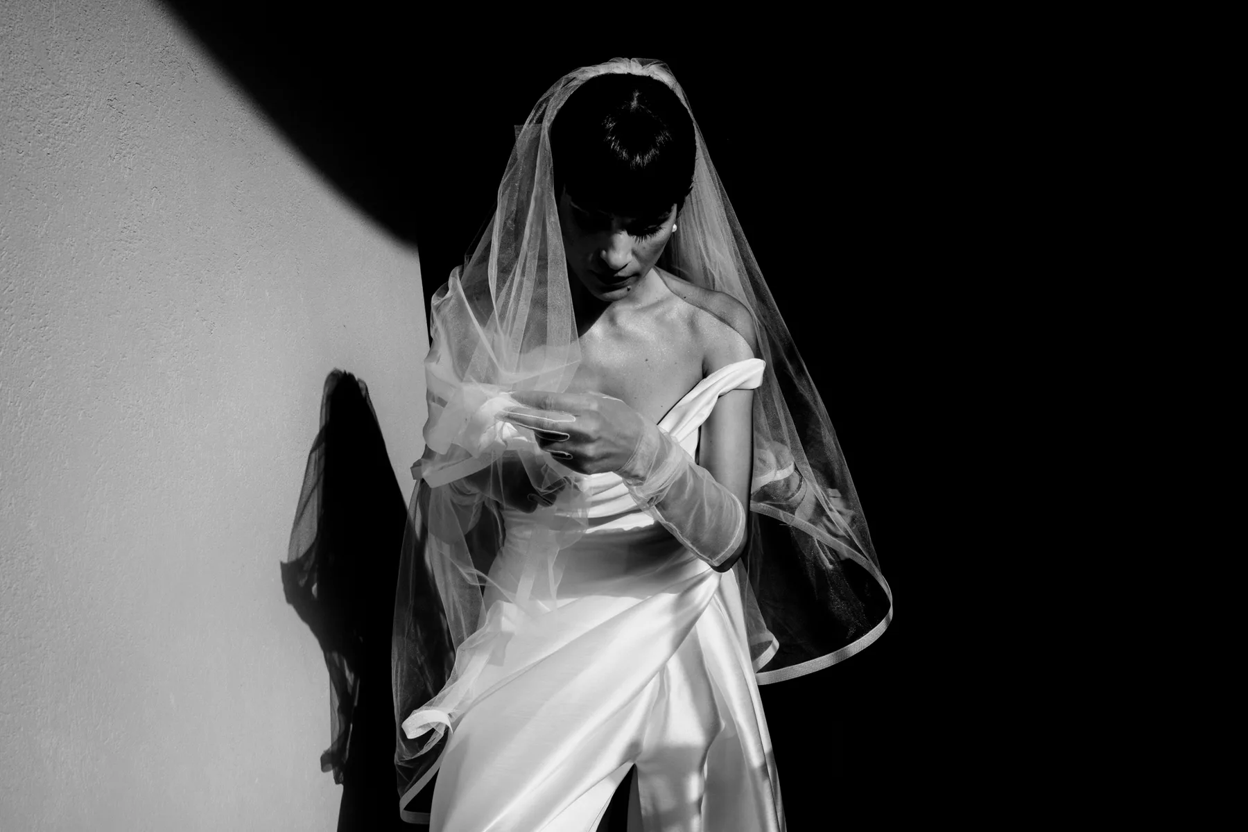 A bride looking down through her veil, half in shadow, in black and white
